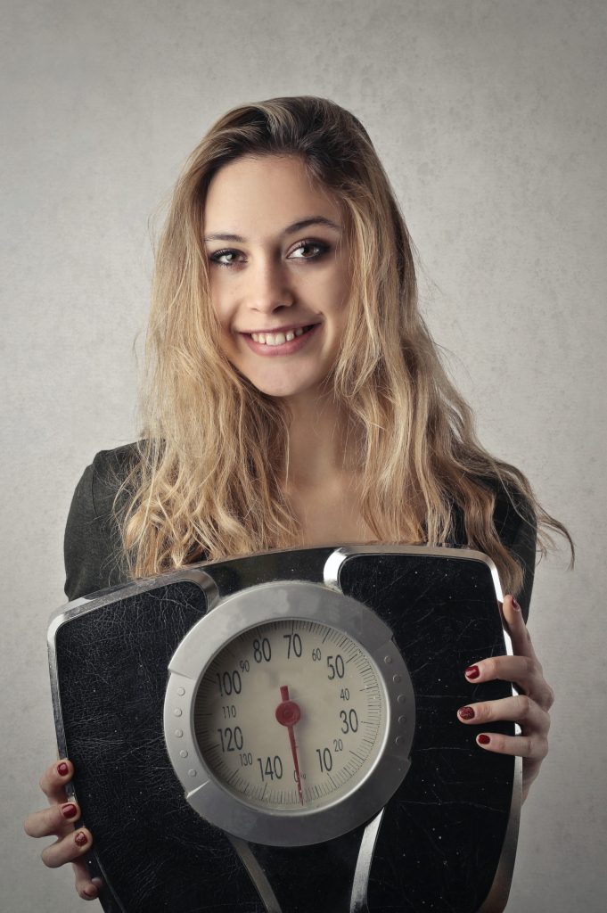 woman smiling and holding scale to show satisfaction with eating disorders, body image, and weight concerns